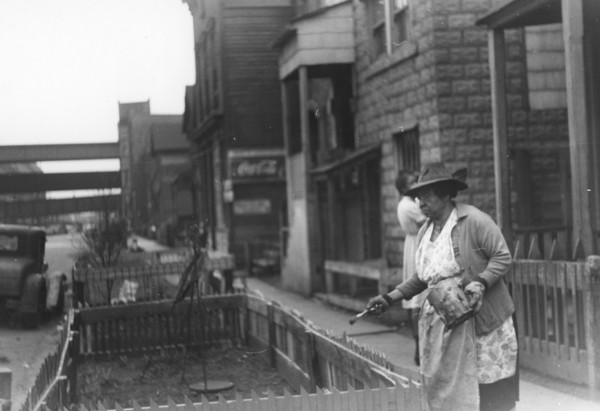 Black woman painting the fence on her "pavement garden," Black Belt, Chicago, Illinois 1941