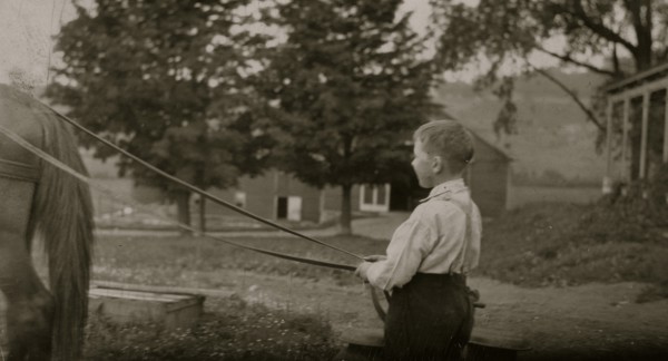 Eight-year old Jack carrying cans of milk on stone boat. This involves some heavy lifting 1915