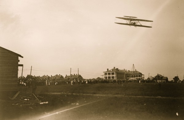 Orville Wright flying in his airplane, crowd on field 1908