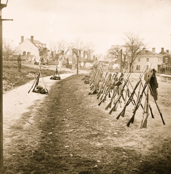 Petersburg, Va. Row of stacked Federal rifles; houses beyond 1865