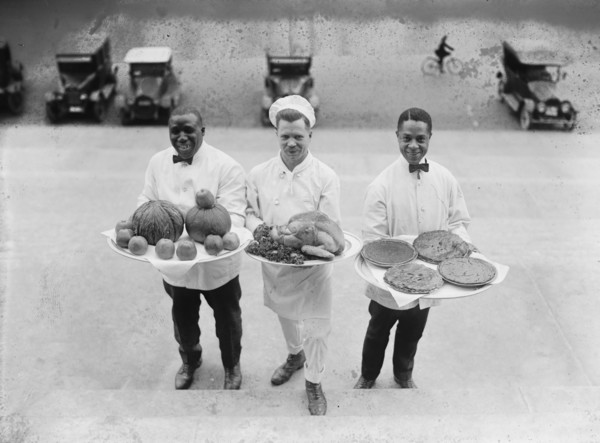 Three Chefs stand on bottom of a line of steps and hold up Thanksgiving platters of Pies, apples and a Turkey 1922