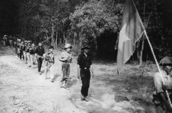 South vietnamese guerrillas file through the jungle along the ho chi minh trail, the flag with a yellow star on a red and blue background is always carried into battle, vietnam war, mid 1960s.