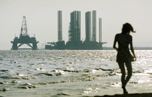 A woman in silhouette walking along shikhov beach on the shore of the caspian sea with an off-shore oil rig under construction in the background, baku, azerbaijan, october 2002.