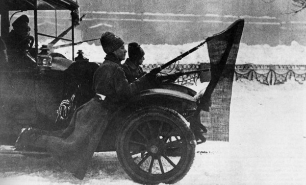 Soldiers traveling on the mudguard auto with red flags fixed to their bayonets. Pietrograd. 1917