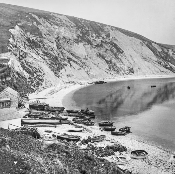 Fishing village on Lulworth Cove with boats on the shore and cliffs along the coast