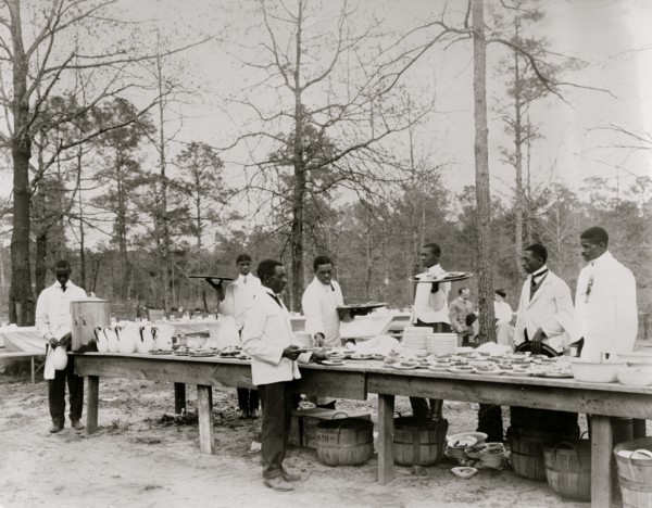 African American men preparing to serve a meal in an outdoor setting among trees