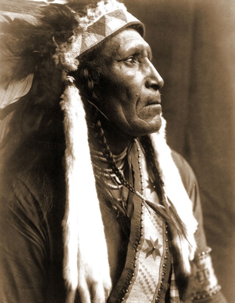 Edward S. Curtis Native American Indians - Raven Blanket, wearing several necklaces and warbonnet with ermine streamers circa 1910.