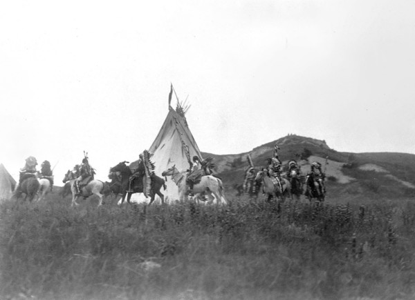 Edward S. Curits Native American Indians - Several Dakota men on horseback riding in a circle around a tipi circa 1907.