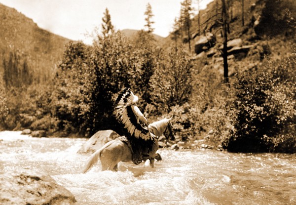 Edward S. Curtis Native American Indians - Bullchief, wearing warbonnet, crossing shallow rapids on horseback circa 1905.