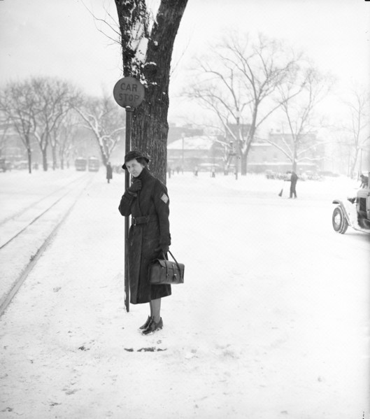 Woman standing in the snow underneath a 'car stop' sign circa 1936.
