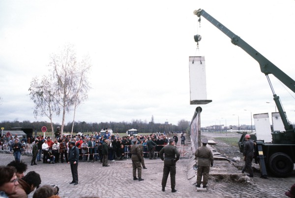 East German police and West German citizens watch as a workman dismantles a section of the Berlin Wall at Potsdamer Platz..