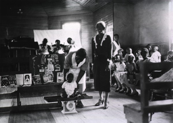 Preschool child is weighed by African American nurse