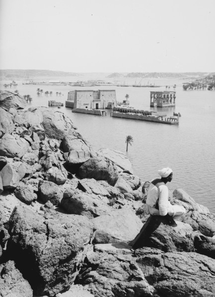 General view of Island of Philae, man sitting on a rock, looking at water ca. 1900