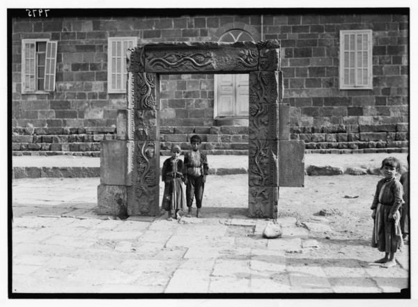 Children standing beneath an ornamented doorway on the town square in Kanawat. Carving of grapevine pattern ca. 1938