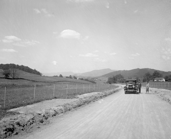 Two men standing outside an automobile on a rural road ca.  between 1910 and 1926
