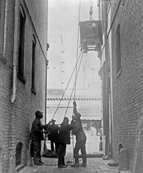 Three African American men lifting a piece of equipment, with block and tackle, at the Standard Engraving Company ca. 1909