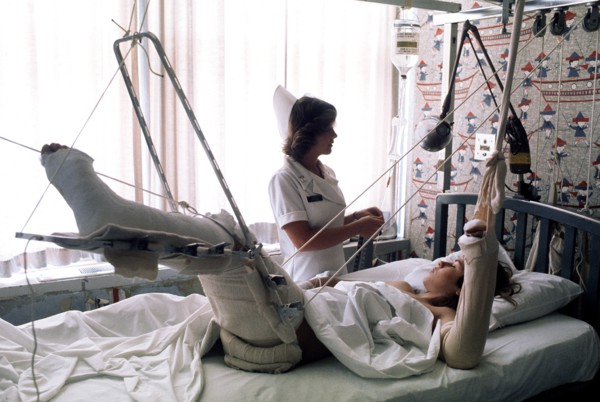 A nurse adjusts the intravenous feeding line on a patient lying in traction