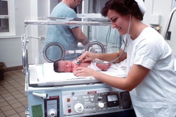 A nurse examines an infant in an incubator.