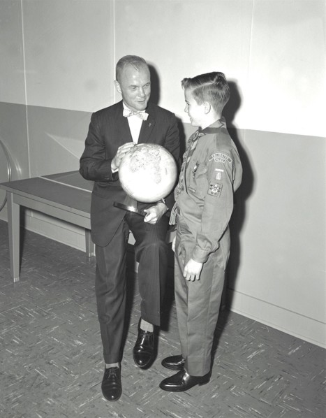 Mercury astronaut John Glenn holding a globe while talking with young boy, a boy scout or cub scout.