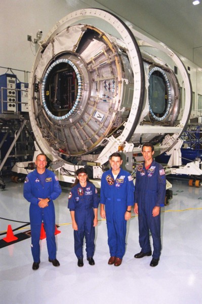 Members of the STS-88 crew pose with the Node 1 of the International Space Station in the high bay of the Space Station Processing Facility ca. 1997