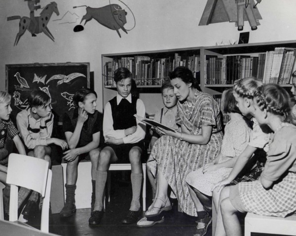 Employee reads stories to a group of youngsters in the children's day room of the Amerika Haus, Hamburg.
