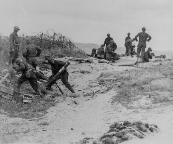 A mortar crew stands back just before firing into a Nazi position somewhere along the Normandy Coast, France.