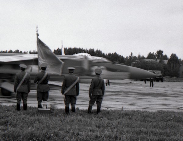 Four officers with regimental banner stand against the MiG-23 taxiing out for takeoff, air base Kubinka, USSR.