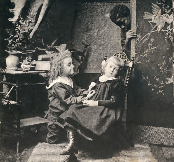 A boy and a girl with a black man looking on from behind a screen.