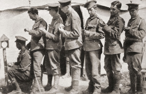 Soldiers during World War One sychronising their watches with a clock mounted on a post in the camp.