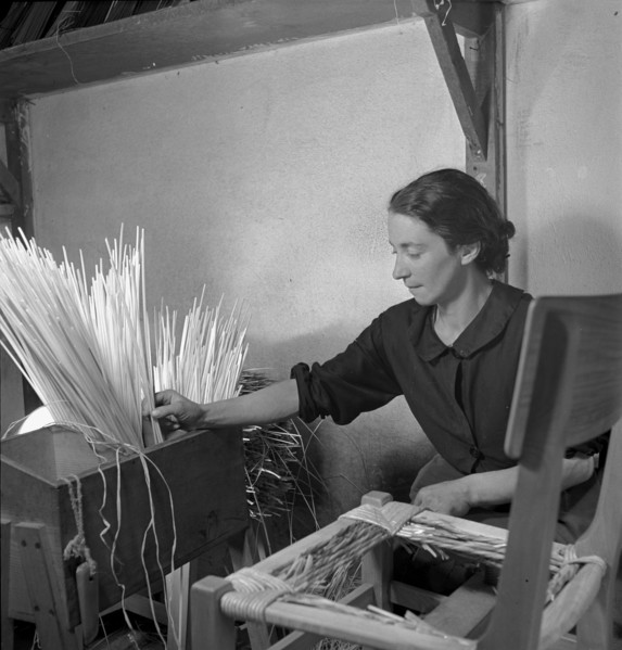 Woman braiding straw around a chair, 1940