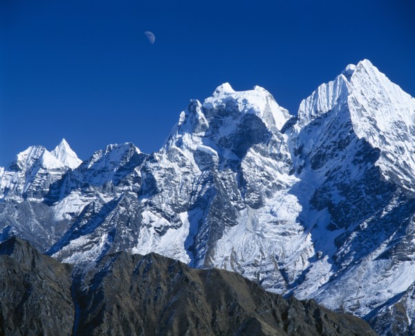 NEPAL, Sagarmatha National Park, Himalayan mountain peaks with moon above just visible in deep blue