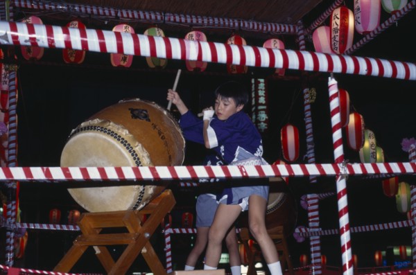 JAPAN, Honshu, Tokyo, Young boy in costume beating a large drum at the O-Bon festival