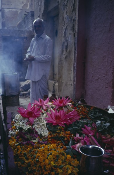 INDIA, Uttar Pradesh, Varanasi, Man standing by display of flowers and burning incense