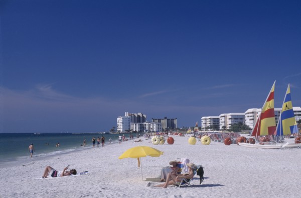 USA, Florida, St.Petersburg, Woman reading under a multicoloured parasol on a sandy beach with