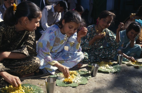 INDIA, Himachal Pradesh, Kulu, Girls eating from banana leaves with their hands at meal during