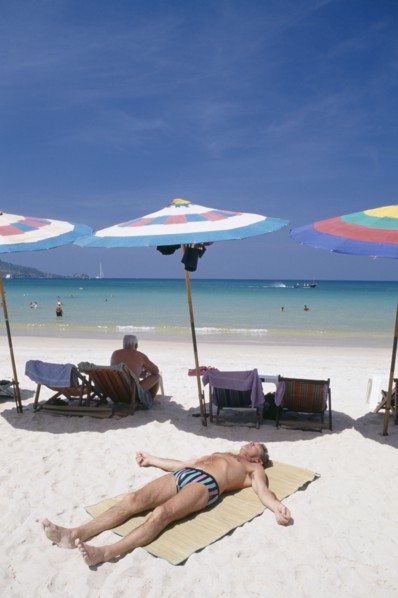 THAILAND, Phuket, Patong Beach, Sun bather lying on the sand in the foreground with row of