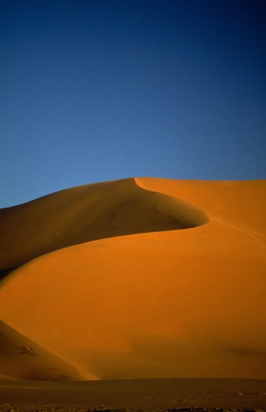 LIBYA , South West, Achan , Orange desert sand dune against a clear blue sky