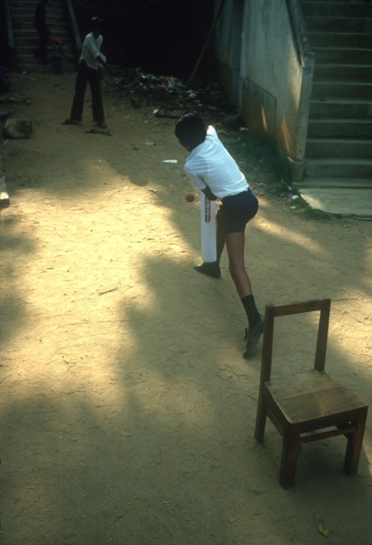 SRI LANKA, Kandy, Young boys playing Cricket in street using a wooden chair as stumps