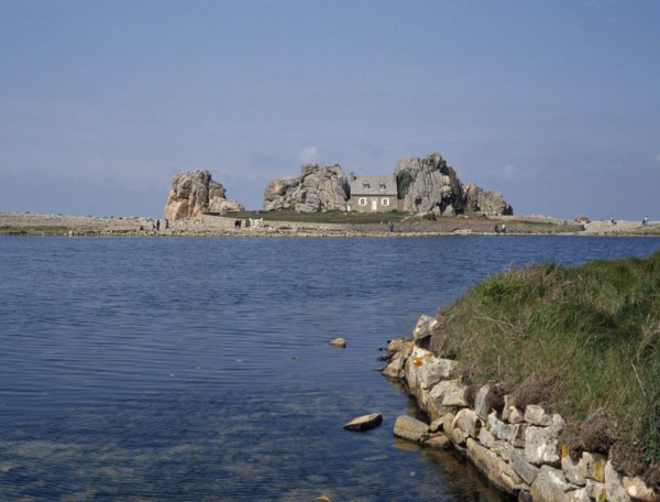 FRANCE, Brittany , Plougrescant, Overlooking an expanse of water to a house surrounded by rocks.