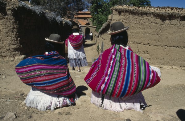 BOLIVIA, Lake Titicaca, Isla del Sol, Yumani Villagers carrying brightly coloured bundles over