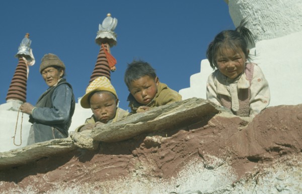 CHINA , Tibet , Catsall , Three children looking down over wall with elderly woman standing behind.