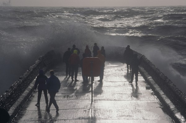 ENGLAND, East Sussex, Brighton, Waves crashing over a groyne with people on it