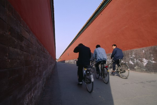 CHINA, Hebei, Beijing, Imperial Palace with cyclists riding down a long red alleyway