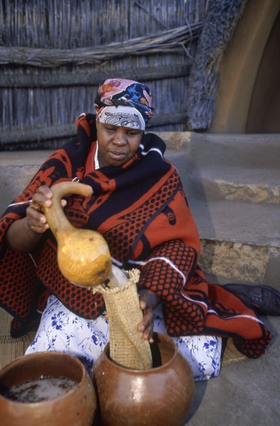 SOUTH AFRICA, Qwa Qwa, Basotho Cultural Village, Basotho woman pouring beer into a strainer from a