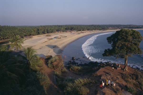 INDIA, Kerala, Bekal, View along the beach and coastline with people standing by tree on rocky