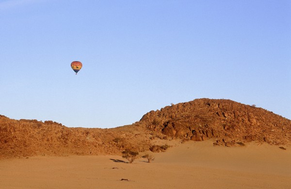 NAMIBIA, Namib Desert, Hot air ballooning above rocky outcrop over sand dunes