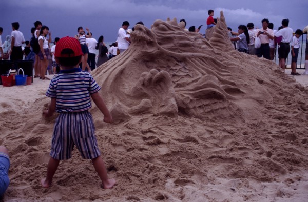 SINGAPORE, Beach, Sand sculpture of a Dragon with a boy standing in front of it holding a handful
