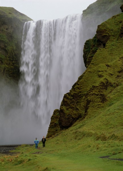 ICELAND, Skogafoss Waterfall, Cascading waterfall 60 metres or 200 feet high.  Two people walking