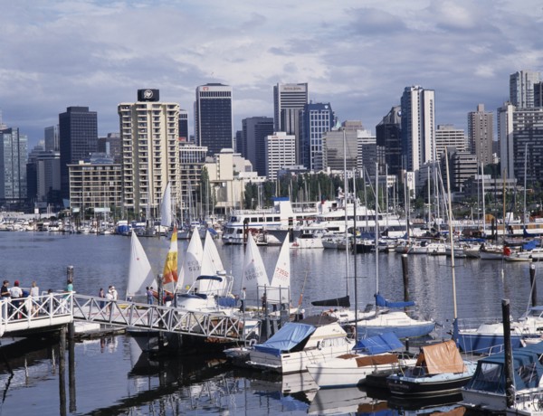 CANADA, British Columbia, Vancouver, City skyline over busy yacht harbour with people walking on