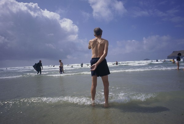 ENGLAND, Cornwall, Polzeath, Man standing in shallow water on the beach looking out to bathers in